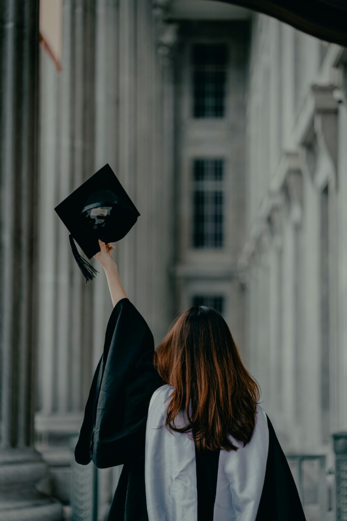Graduada levantando un birrete frente a un edificio académico, representando compromiso personal con los estudiantes